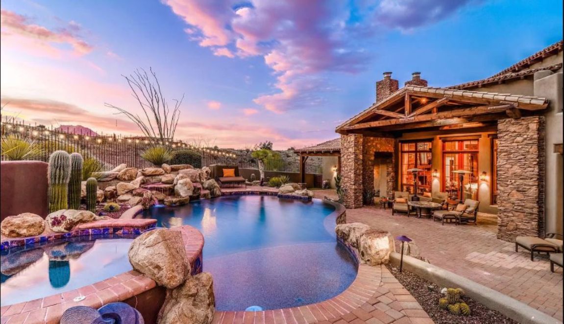 Eagles Nest Southwest Ranch backyard at sunset with curved swimming pool, rock waterfall and covered stone patio