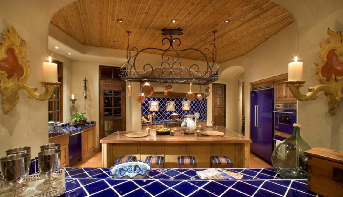 Mirabel Hacienda kitchen with vivid blue tile, wood cabinetry, large island and decorative wrought-iron pot rack