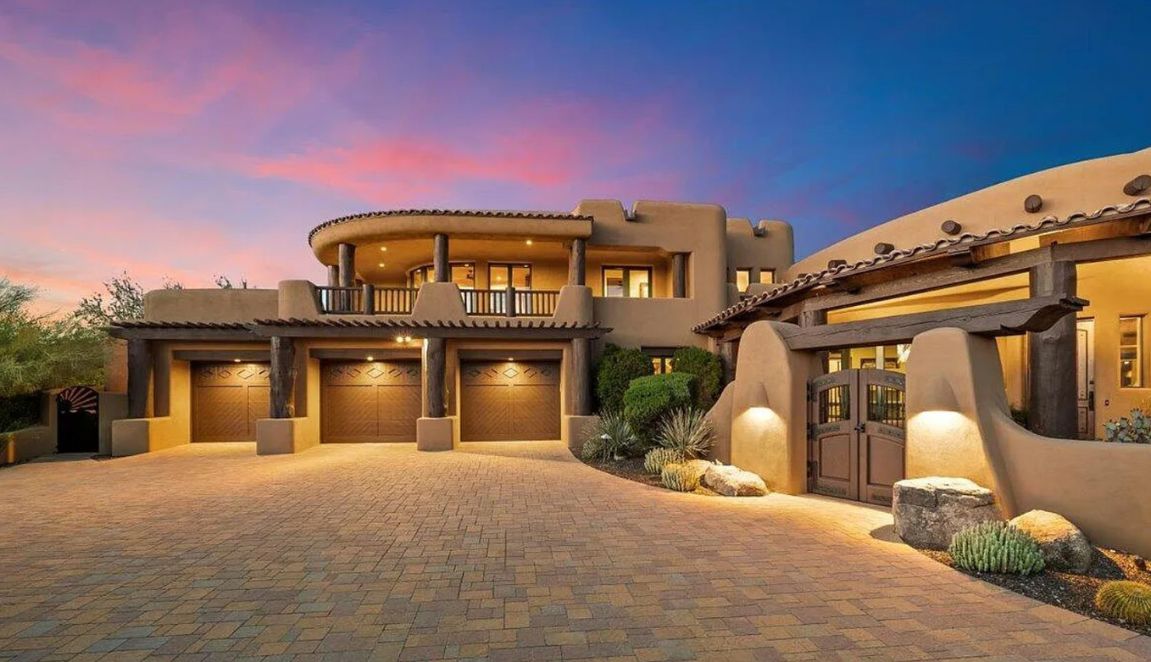 DC Ranch Pueblo front exterior at sunset with three-car garage, rounded stucco forms and timber details